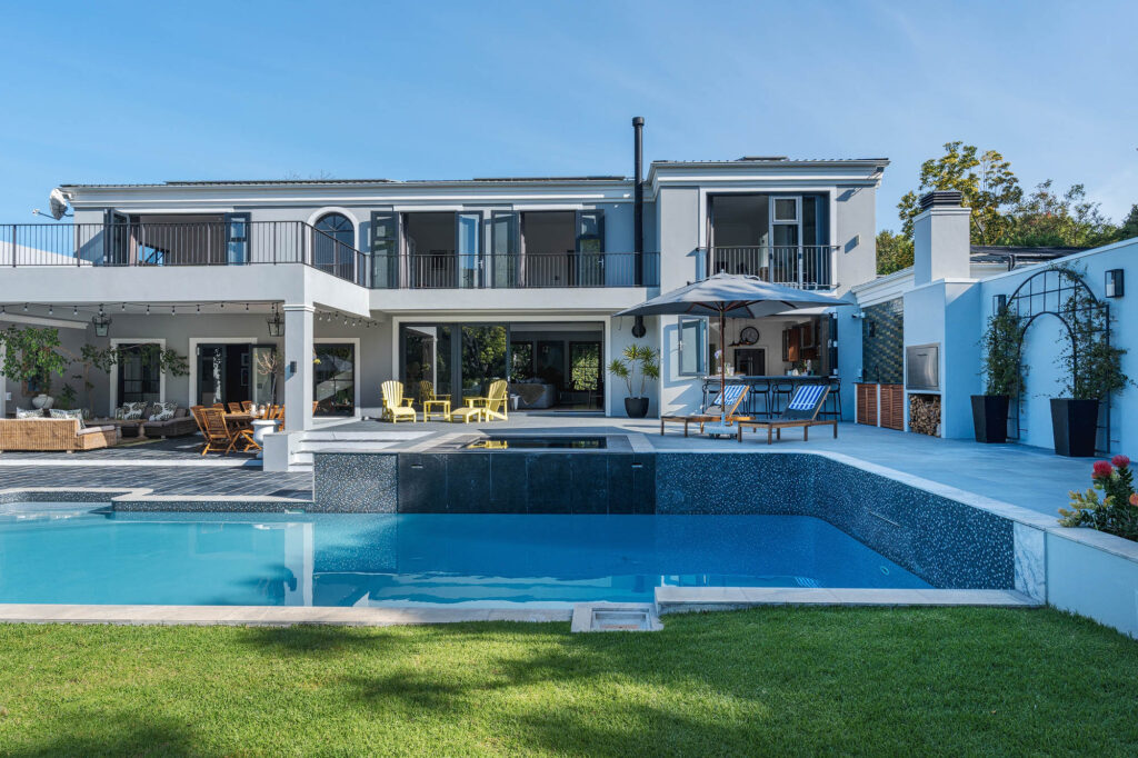 A sparkling heated swimming pool surrounded by lush greenery, with lounge chairs and umbrellas offering a relaxing outdoor retreat.