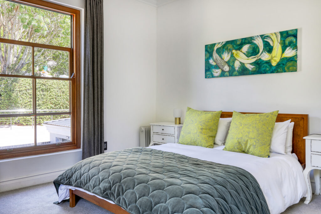 A spacious and elegantly designed bedroom, soft neutral tones, large windows offering natural light