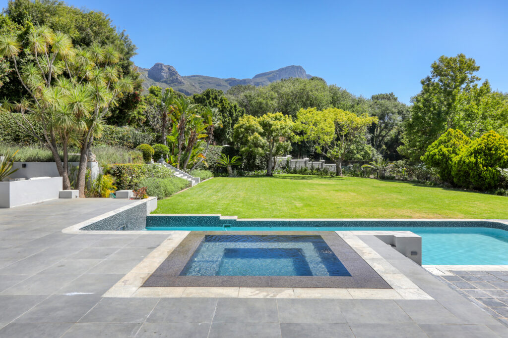 A sparkling heated swimming pool surrounded by lush greenery, with lounge chairs and umbrellas offering a relaxing outdoor retreat.