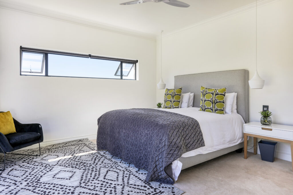 A spacious and elegantly designed bedroom, soft neutral tones, large windows offering natural light